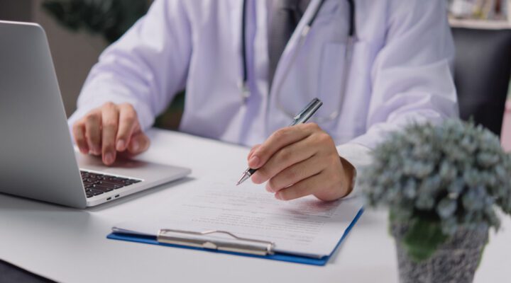 form being filled by doctor while working on laptop